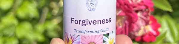 A bottle of Crystal Herbs Forgiveness flower and crystal essence combination in front of flowers